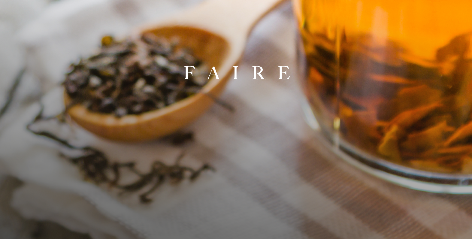 A close-up shot shows a wooden spoon filled with loose-leaf tea next to a glass of brewed amber-colored tea. The word "F A I R E" is subtly overlaid on the image in white text.