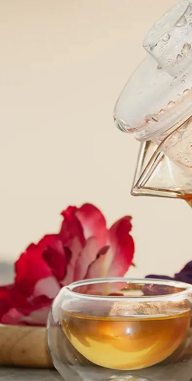 Glass teapot pouring herbal tea into a clear cup with flower, calming caffeine-free wellness tea